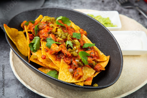 nachos with sauce, meat and herbs in a black plate, side view