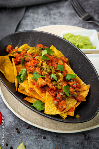 nachos with sauce  meat and herbs in a black plate  side view