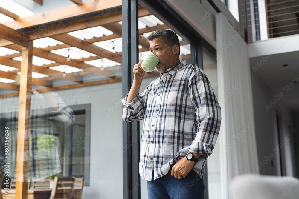 Thoughtful senior biracial man drinking coffee at window at home Thoughtful senior biracial man drinking coffee at window at home