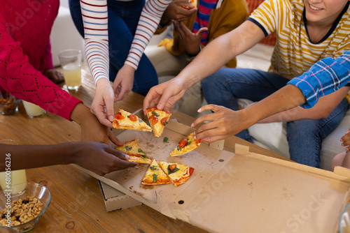 Happy diverse group of teenage friends sitting on couch and sharing pizza photo