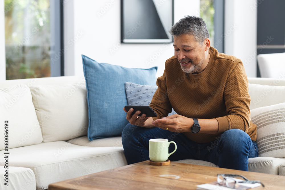 Happy senior biracial man sitting on couch and using smartphone at home Happy senior biracial man sitting on couch and using smartphone at home