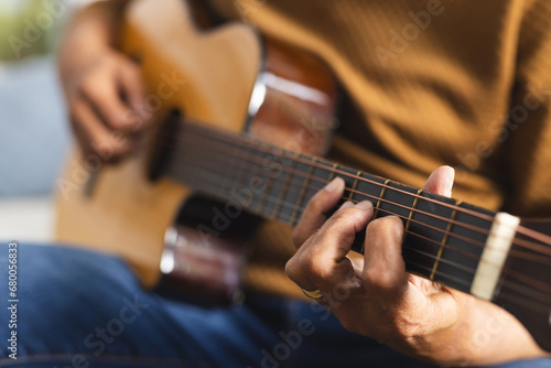 Senior biracial man sitting on couch and playing guitar at home photo