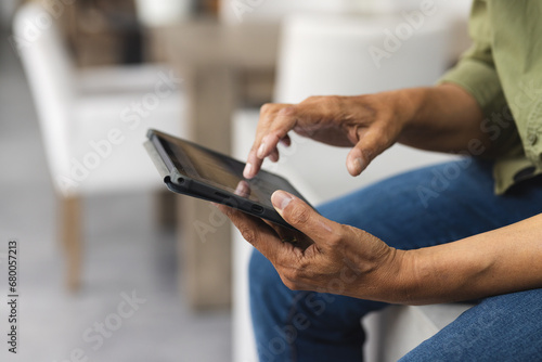 Senior biracial man sitting on table and using tablet at home photo