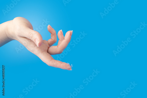Hygiene and optics, soft contact lens for clear sight on the finger closeup, blue background, copy space
