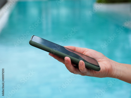 Young woman's hand holding a smartphone Blurred blue pond background