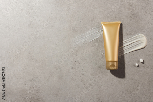 Beauty product gold tube and cream smudges with copy space on stone background