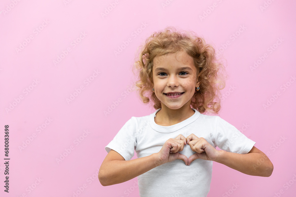 Cute little American girl making heart shape with her hands and smiling to camera, posing over pink background in studio, empty space. Happy female kid folders hands as heart sign, love symbol Cute little American girl making heart shape with her hands and smiling to camera, posing over pink background in studio, empty space. Happy female kid folders hands as heart sign, love symbol