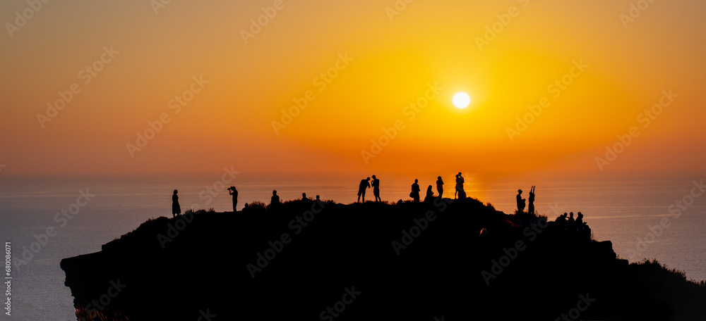 People enjoy sunset on the beach at cliff.