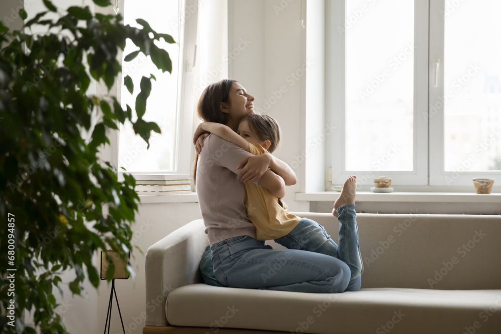 Young beautiful joyful mother shows care, love and attention to little daughter hugging her while sitting on cozy sofa. Happy girl enjoy weekend with mom at home. Happy family, motherhood, childhood Young beautiful joyful mother shows care, love and attention to little daughter hugging her while sitting on cozy sofa. Happy girl enjoy weekend with mom at home. Happy family, motherhood, childhood