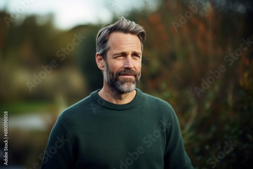 Portrait of a content man in his 40s wearing a cozy sweater against a quiet countryside landscape. AI Generation