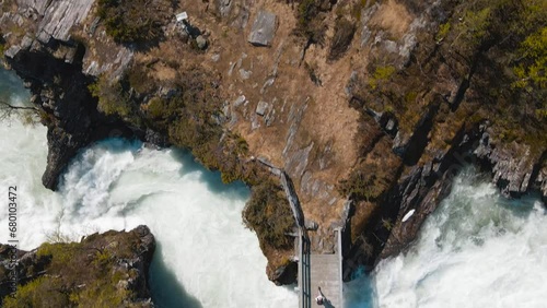 A hiker crosses a fast-flowing river on a wooden bridge. Drone view from above. Billingen, Norway photo