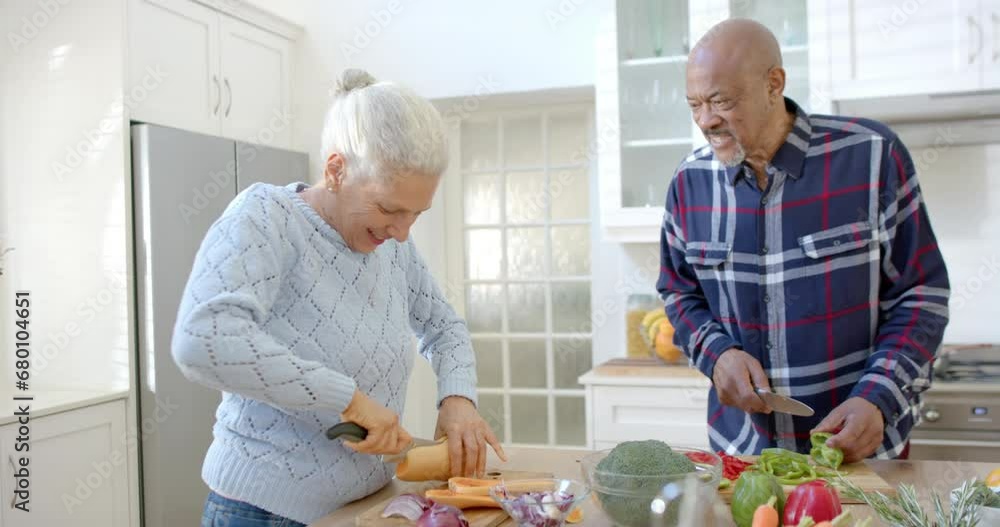 Happy senior diverse couple talking and cutting vegetables in kitchen, slow motion Happy senior diverse couple talking and cutting vegetables in kitchen, slow motion