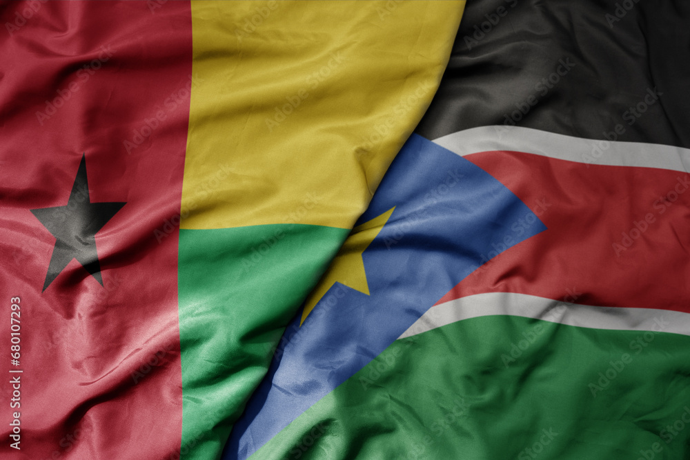 big waving national colorful flag of south sudan and national flag of guinea bissau .