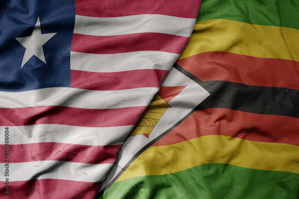 big waving national colorful flag of zimbabwe and national flag of liberia .