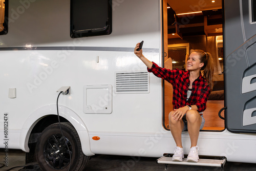 Young woman taking self portrait while sitting in the doorway of recreational vehicle camper van. RV parking lifestyle.