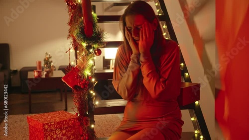 Young crying woman sitting in living room decorated for Christmas or New Year and looking at police lights and sirens. Crime, ambulance, injury, problems with law and theft on winter holidays and cele