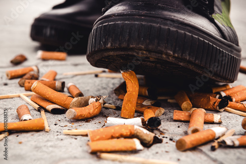 A foot in a shoe extinguishes a burnt cigarette butt. Smoking is harmful to human health. Smoking