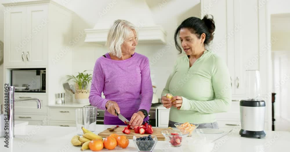Two happy diverse senior women chopping fruits and laughing in kitchen, slow motion Two happy diverse senior women chopping fruits and laughing in kitchen, slow motion