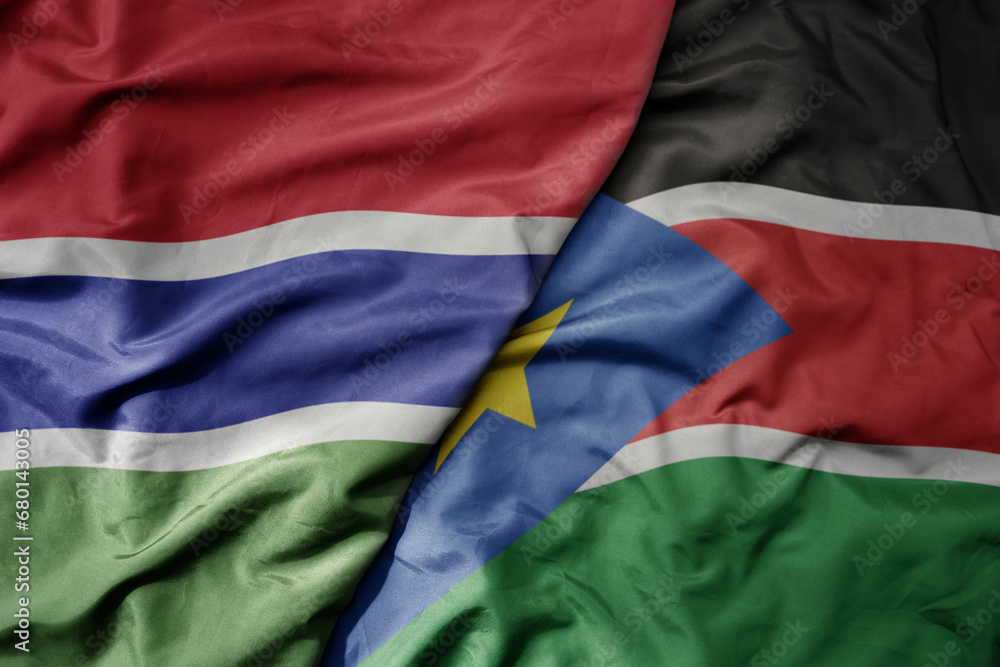 big waving national colorful flag of south sudan and national flag of gambia .