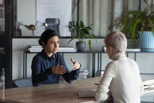 Indian female business mentor training intern, explaining work task to employee. Candidate and employer, recruiter, hr agent talking at job interview, meeting at table, discussing hiring, experience photo