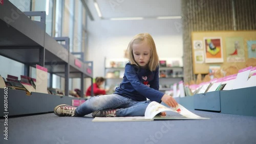 Adorable preschooler girl sitting on the floor in municipal library and reading book photo