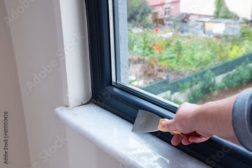 The man is using a putty knife to clean the old insulation from the windowsill. photo