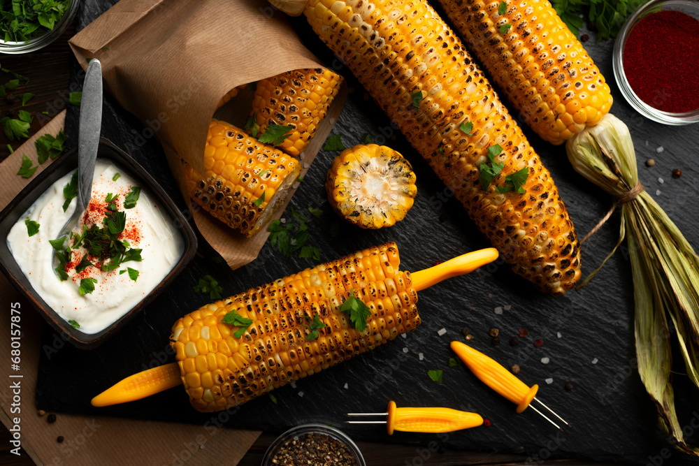 Grilled corn on the cob in caucasian hands on kitchen wooden table background