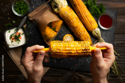 Grilled corn on the cob in caucasian hands on kitchen wooden table background