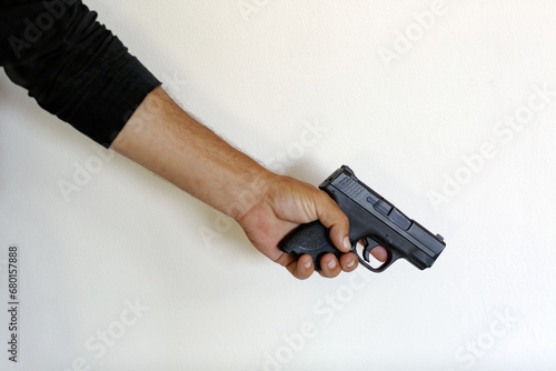 man hand hold a gun on a white wall background. Male hand holding 9mm handgun. Criminal, illegal, killer. Close up of man hand with black pistol, finger on the trigger of the gun. Selective focus