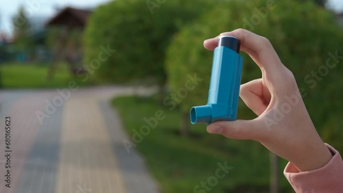 Asthma disease during childhood. A view of asthma inhaler in child hands on park path during day time. photo