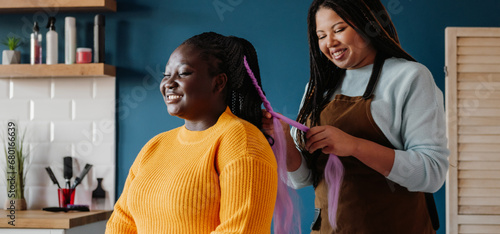 Happy African American hairdresser braiding hair to a female customer in salon photo