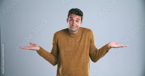 Confused, shrug and face of man in studio with decision, choice and dont know reaction. Thinking, wondering and portrait of person with hand gesture for unsure, doubt and what on blue background photo
