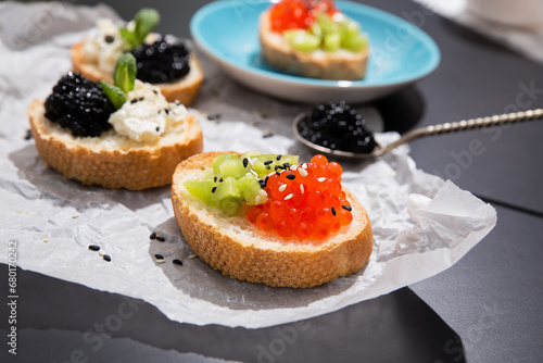 Fusion cuisine concept. Fine dining with caviar appetizer. Fine dining with caviar appetizer, red and black caviar canape of white crispy baguette bread with chopped kiwi fruit and sezame seeds. 