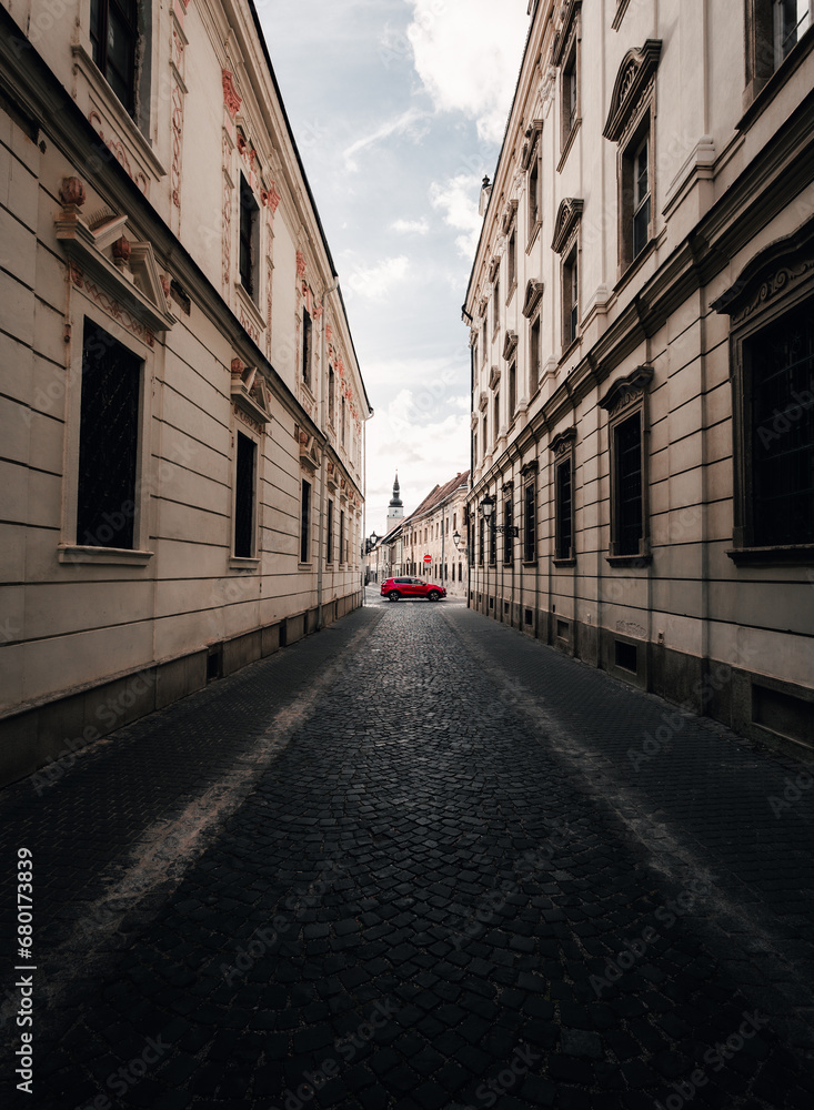 Vertical photo of historic city center in Trnava city - Slovakia. Wide angle shot of old town street in Trnava - taken from the ground with paved walkway on foreground - Urban and street concept.