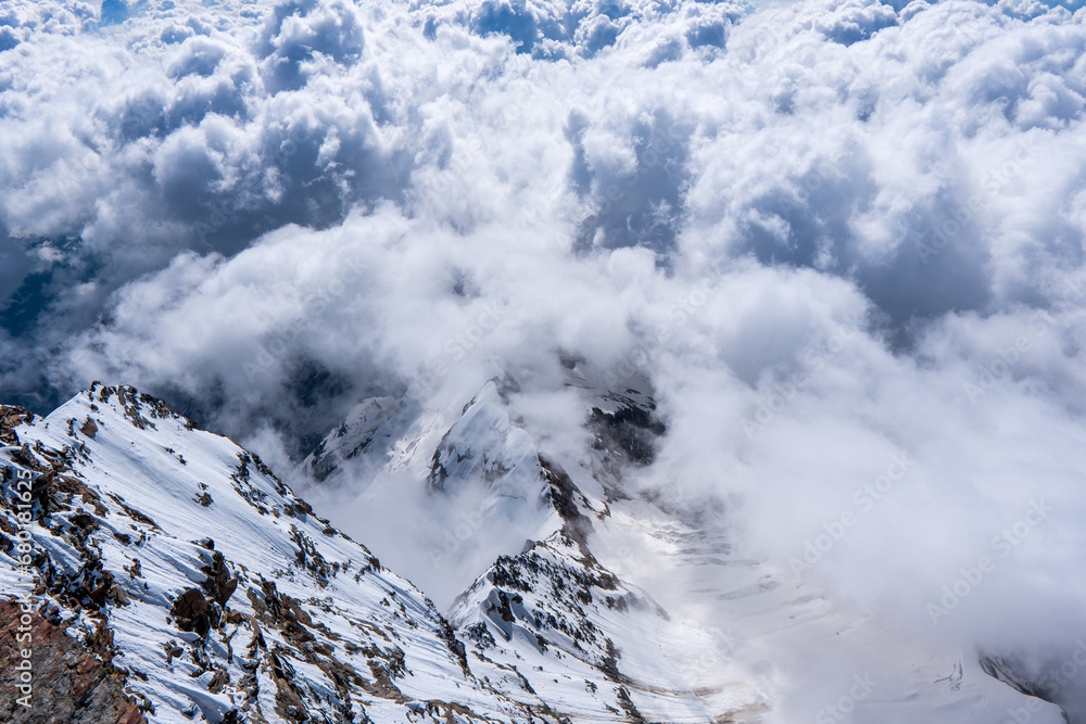 alpine landscape with peaks covered by snow and clouds Cloudy mountains. Mountains in clouds at sunrise in summer. Aerial view of mountain peak with green trees in fog. Top view o