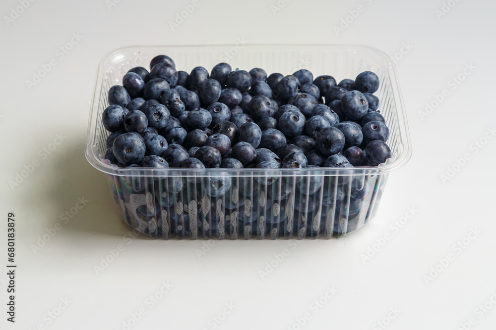 Fresh juicy blueberries and blueberries in a transparent plastic container on a white table Fresh juicy blueberries and blueberries in a transparent plastic container on a white table