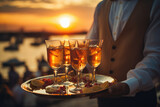 The waiter serves glasses of alcohol on a tray. Summer beach holiday at sunset, with space for text