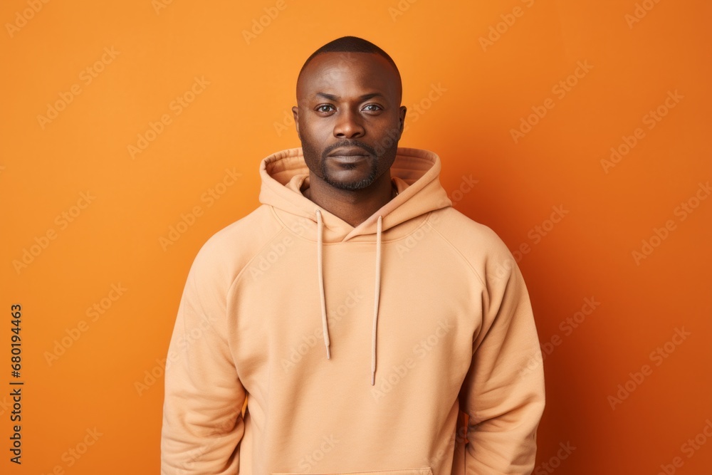 Obraz premium Portrait of a tender man in his 40s sporting a comfortable hoodie against a soft orange background. AI Generation