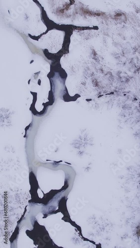 Aerial view of a winter landscape with a frozen river in the mountains with  flowing water in Canada (ID: 680200844)