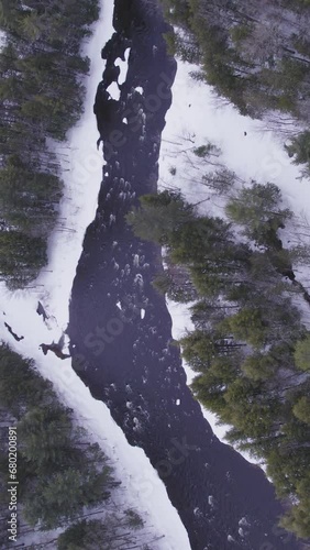 Aerial view of a winter landscape with a frozen river in the mountains with  flowing water in North America (ID: 680200891)