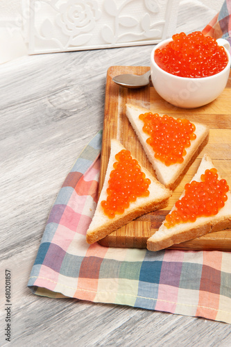 toasts with red caviar and butter on a wooden board with a checkered towel