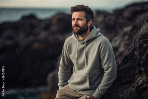 Portrait of a blissful man in his 30s sporting a comfortable hoodie against a rocky shoreline background. AI Generation