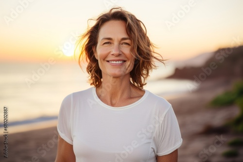 Portrait of a happy woman in her 40s dressed in a casual t-shirt against a vibrant beach sunset background. AI Generation