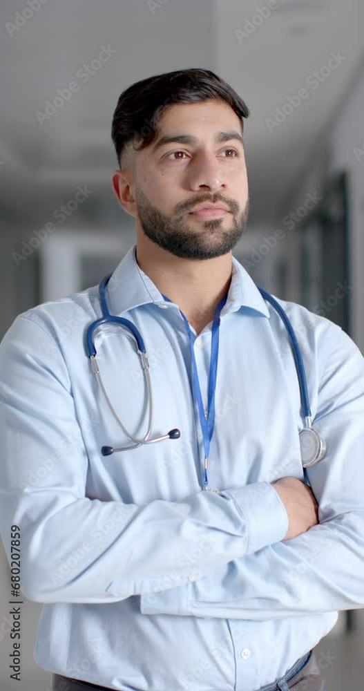 Vertical video of portrait of happy biracial male doctor in hospital corridor, slow motion Vertical video of portrait of happy biracial male doctor in hospital corridor, slow motion