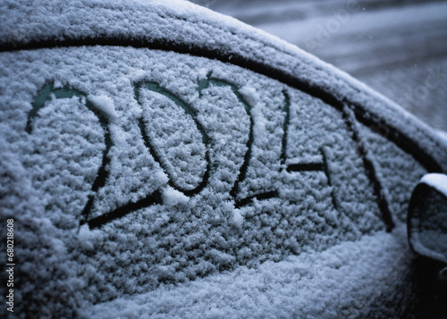 Snow on the car where the numbers are written 2024. New Year concept.