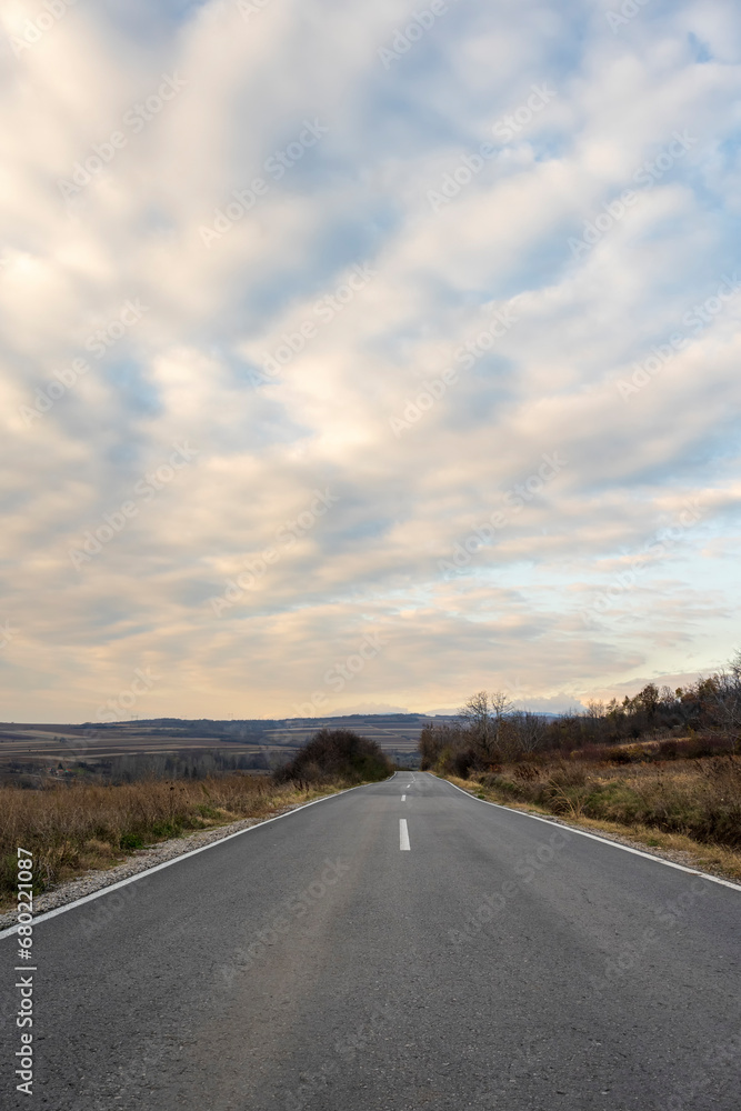 New country road in autumn.  Country road cutting through green fields in the countryside. Empty asphalt road in rural landscape with dramatic clouds. Open Road.  