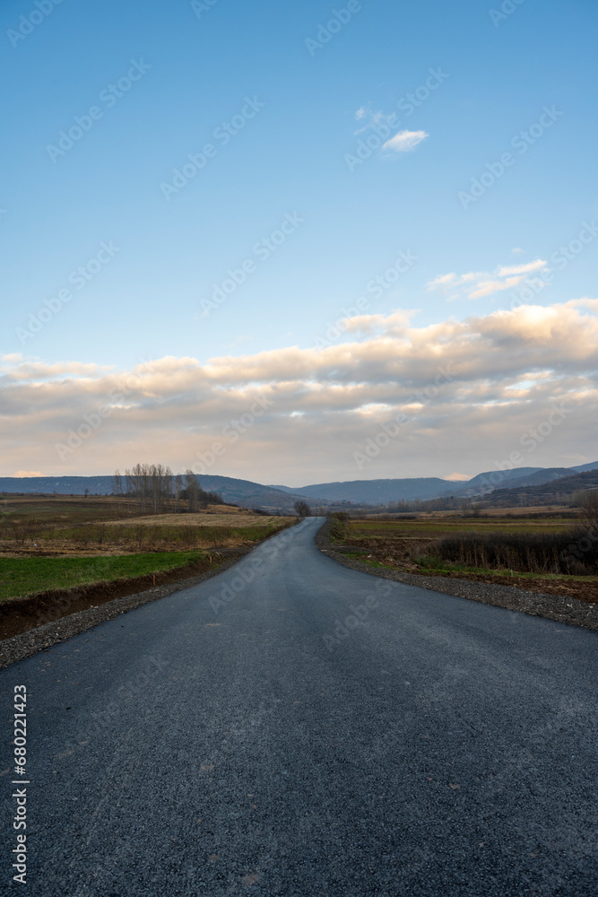 New country road in autumn.  Country road cutting through green fields in the countryside. Empty asphalt road in rural landscape with dramatic clouds. Open Road.  