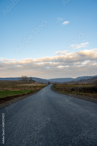 New country road in autumn. Country road cutting through green fields in the countryside. Empty asphalt road in rural landscape with dramatic clouds. Open Road. 