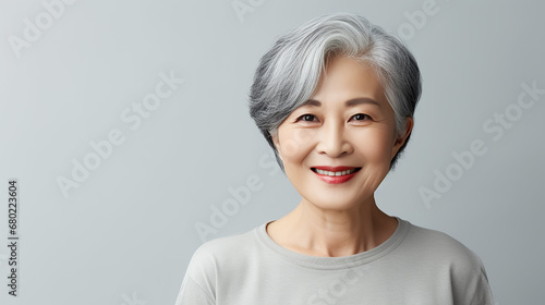 Portrait of asian lady, senior woman with grey hair smiling and looking at camera, standing over grey background.
