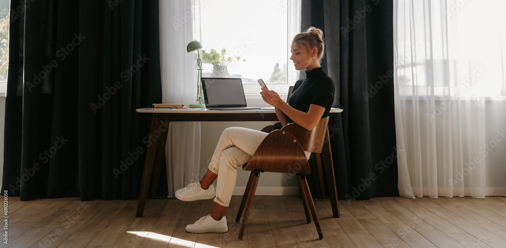 Confident young businesswoman using smart phone while working at home front of the window Confident young businesswoman using smart phone while working at home front of the window